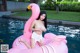 A woman in a white bikini sitting on an inflatable flamingo.