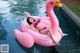 A woman in a pink bikini laying on an inflatable flamingo.