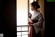 A woman in a kimono holding a fan by a window.